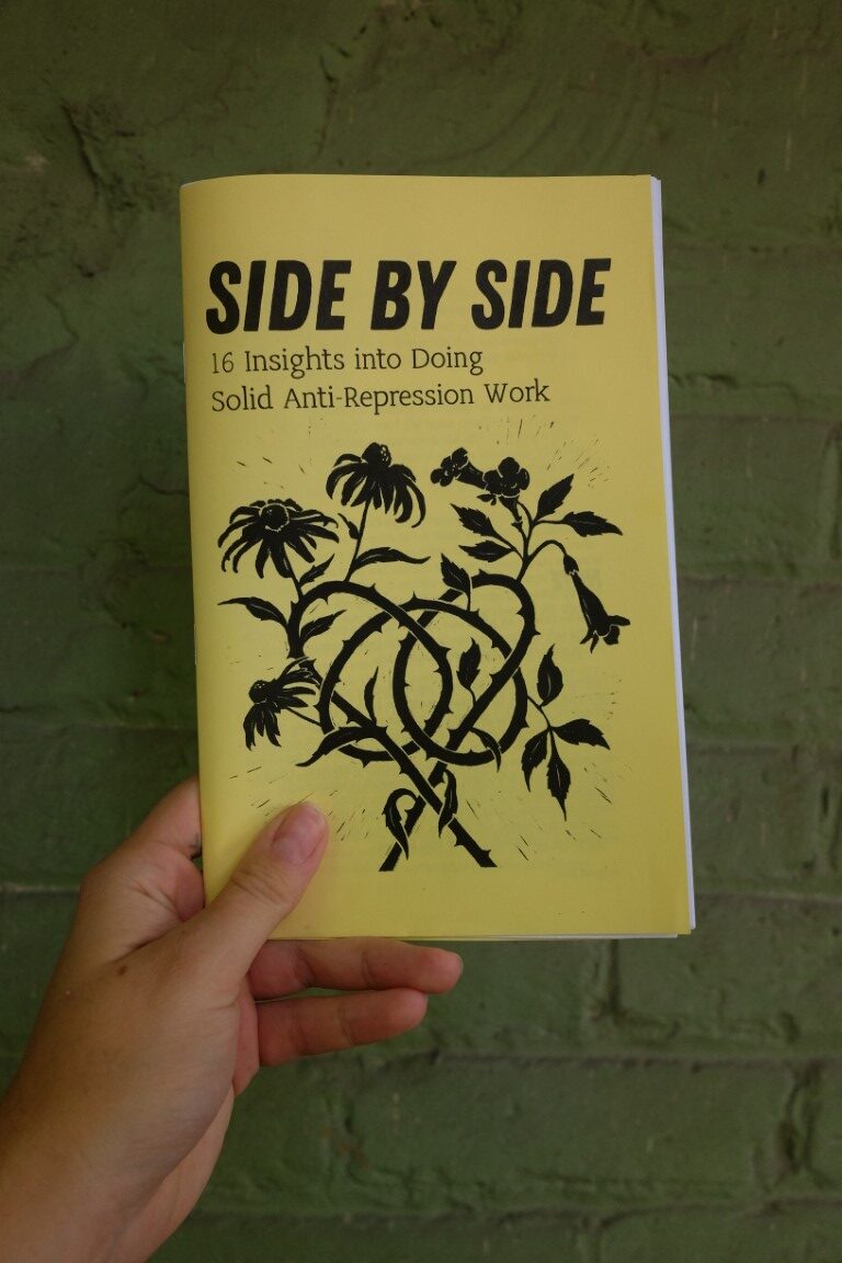 the zine "side by side: 16 insights into doing solid anti-repression work". the zine is printed on yellow paper and the cover illustration is a block print style image of flowers with intertwined spiky stems.